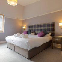 Spacious hotel room with plush bed, cosy plaid headboard, and scenic window view.