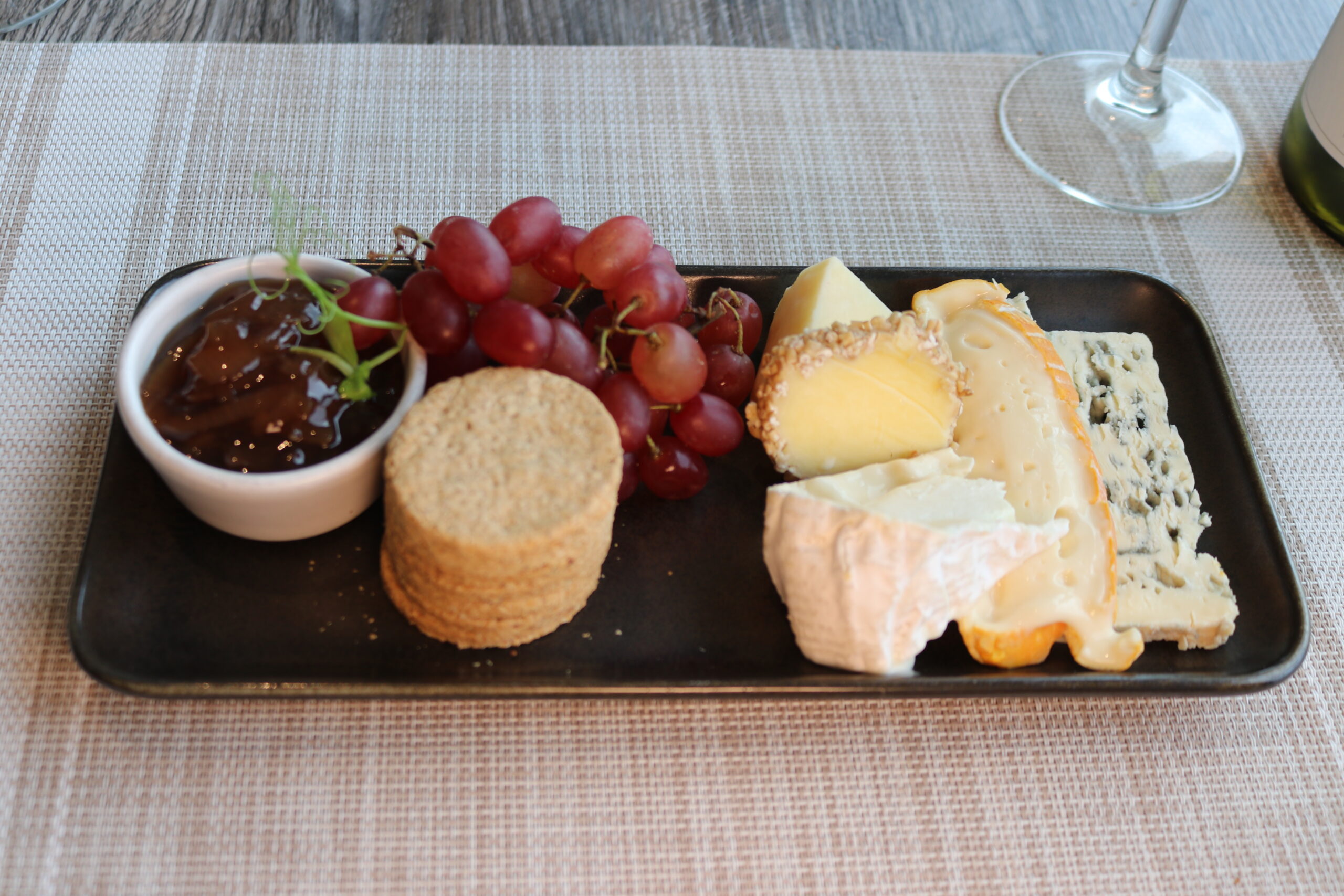 A delicious cheese platter with grapes, chutney, and crackers on a restaurant table setting.