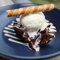 Rich chocolate dessert with vanilla ice cream and wafer, served in a blue bowl outdoors.