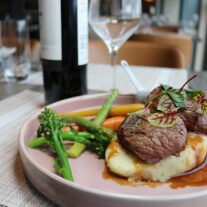 Gourmet beef dish with vegetables, served in a cosy hotel dining room with wine.