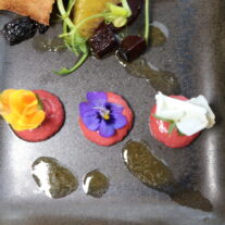 Gourmet appetisers with edible flowers elegantly presented on a dark plate.