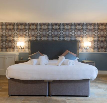 Cosy hotel room with a large bed, decorative wallpaper, and soft lighting, creating a welcoming atmosphere.