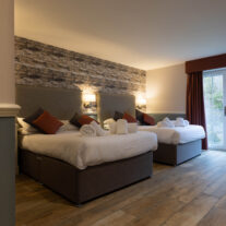 Cosy double room with two beds, warm lighting, and a view through glass doors to nature.
