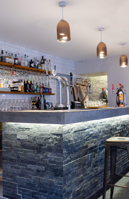 Cosy hotel bar with stone counter, inviting seating, warm lighting, and a wide selection of spirits.