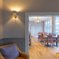 Elegant hotel lounge with cosy armchair, soft lighting, and inviting dining area views.