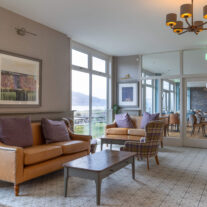 Inviting hotel lounge with cosy sofas, large windows, and scenic view of hills and water.