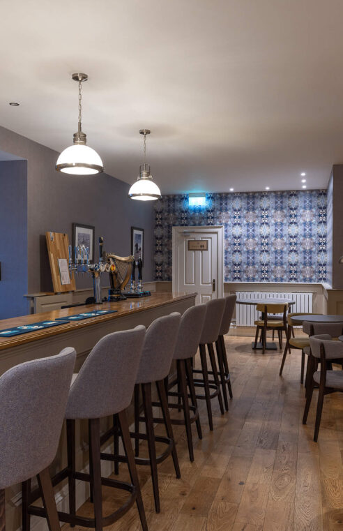 Cosy hotel bar with soft lighting, wooden flooring, and seating for social gatherings.