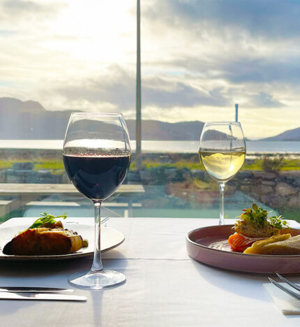 Scenic dining setup with wine and gourmet meals by a window overlooking a serene lakeside view.