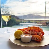 Fresh seafood and white wine on a table, overlooking serene coastal scenery at Balmacara hotel.