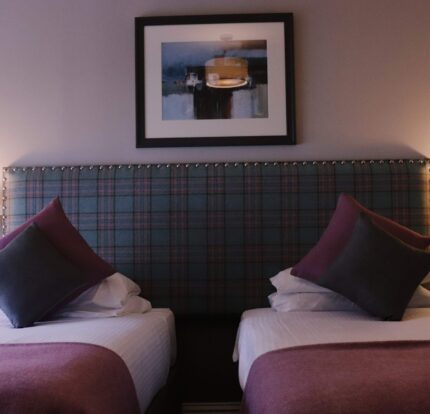 Cosy twin beds with plush pillows and warm lighting in Balmacara hotel room.
