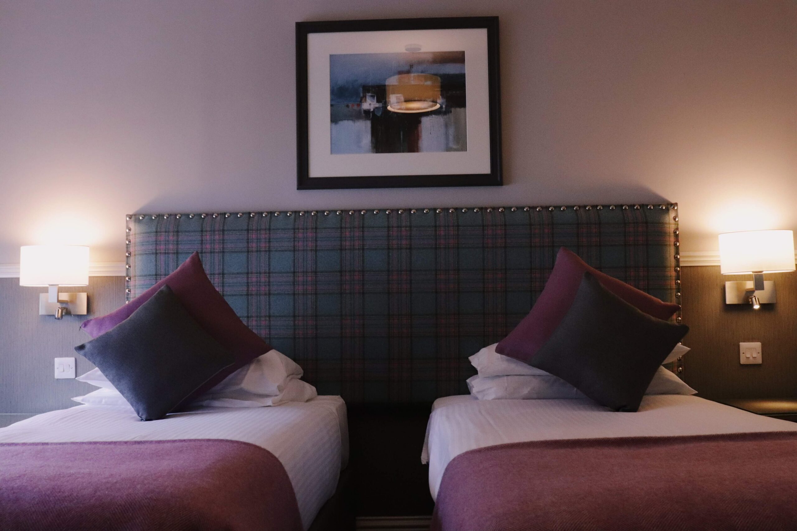 Cosy twin beds with plush pillows and warm lighting in Balmacara hotel room.