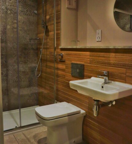 Modern hotel bathroom with wooden accents, featuring a sleek shower and a round mirror.