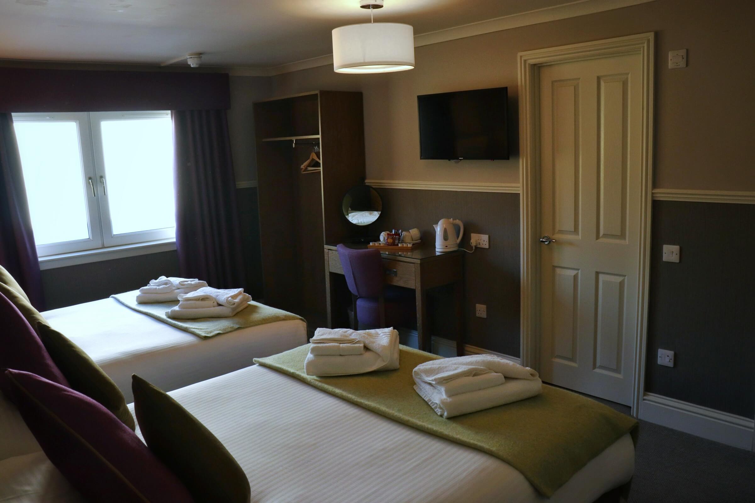 Cosy hotel room with twin beds, neatly folded towels, and a scenic window view.