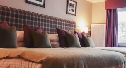 Cosy hotel room with a large bed, soft pillows, and warm lighting in Balmacara.