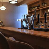 Cosy hotel bar with wooden counter, beer taps, and inviting seating arrangement.