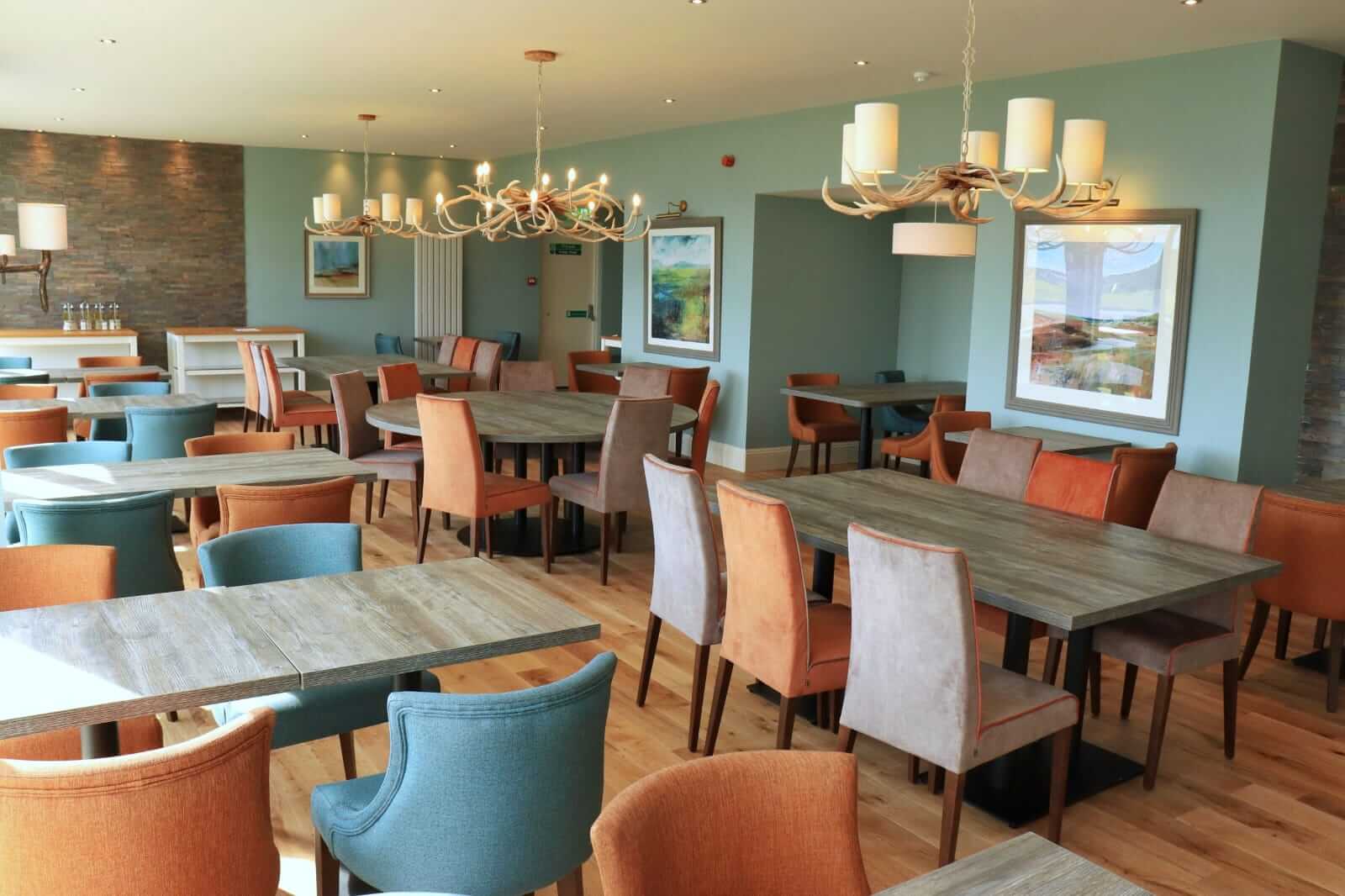 Bright dining area with colourful chairs, wooden tables, and antler chandeliers in Balmacara hotel.