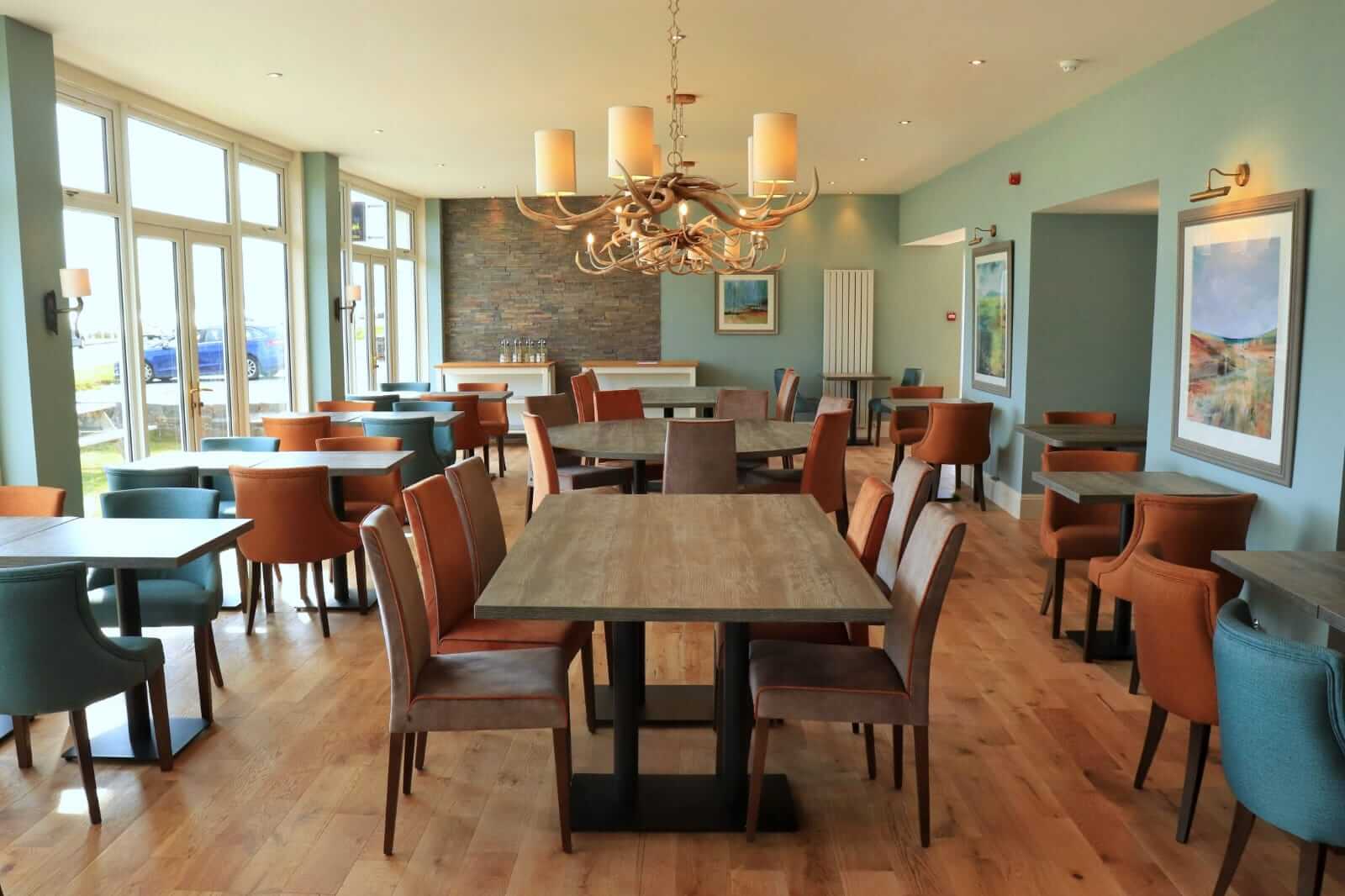 Inviting hotel dining area with colourful chairs, large windows, and elegant chandelier.
