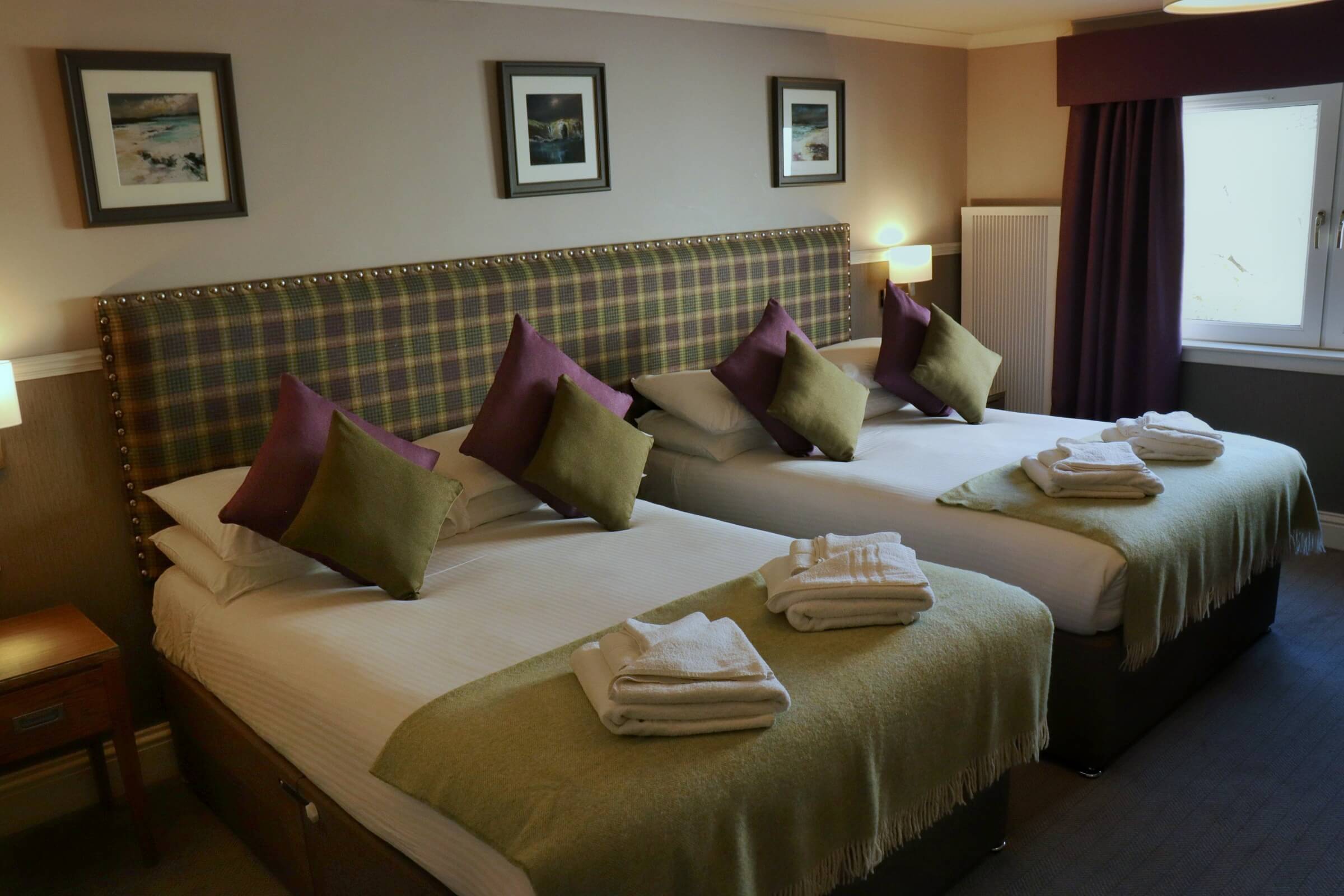 Cosy hotel room with two double beds, green and purple cushions, and warm lighting.