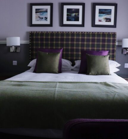 Cosy hotel room with plush bed, green and purple decor, and elegant framed art above the headboard.