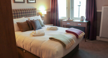 Cosy hotel room with a plush bed, colourful throws, and a tea set near the window.