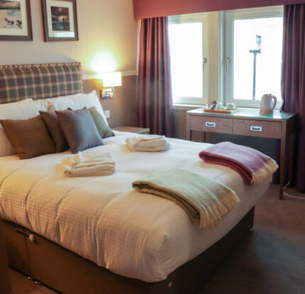 Cosy hotel room with a plush bed, colourful throws, and a tea set near the window.