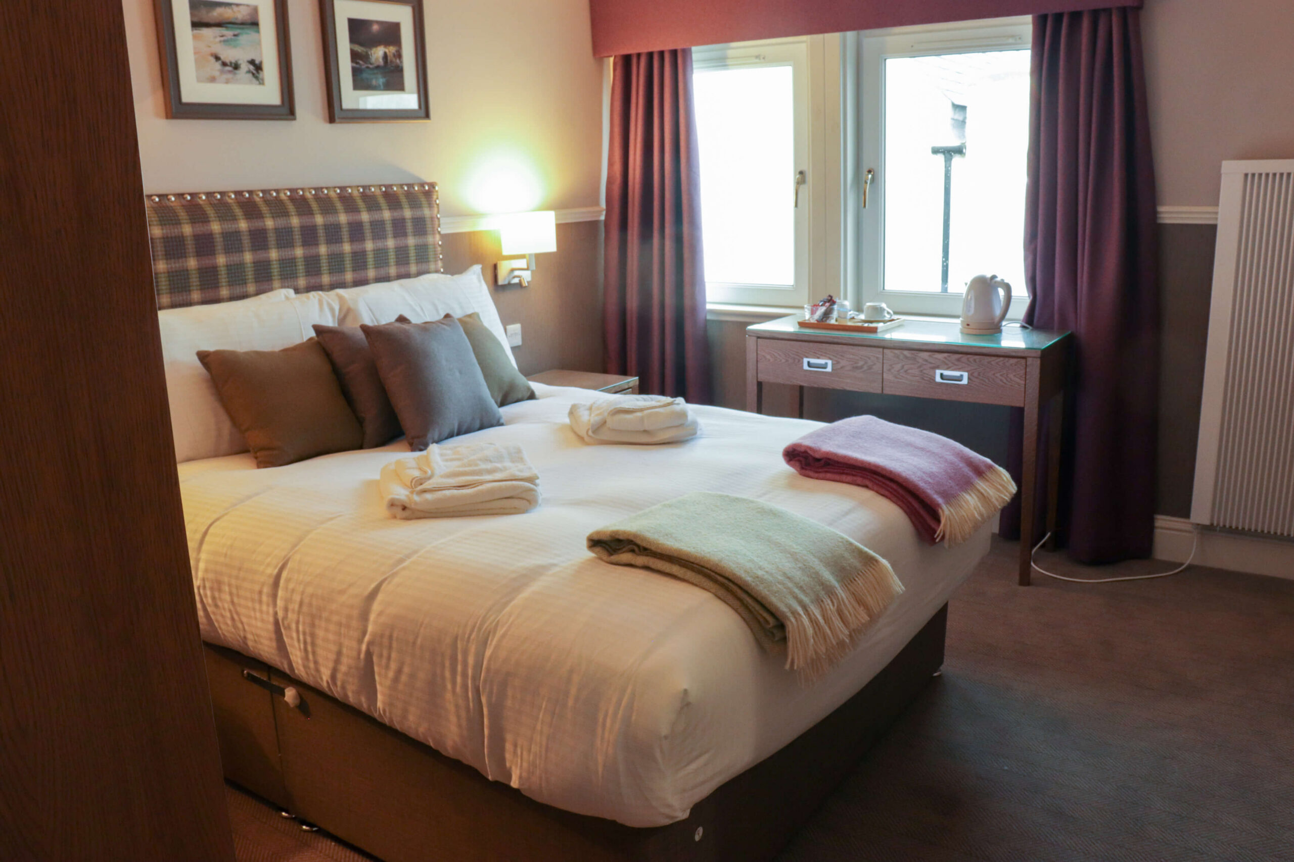 Cosy hotel room with a plush bed, colourful throws, and a tea set near the window.