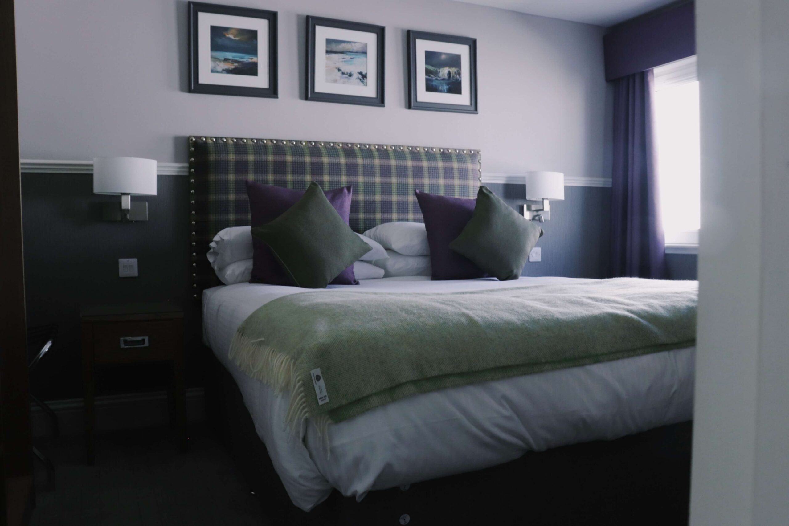 Cosy hotel room with a tartan headboard, plush pillows, and soft lighting, inviting and serene.