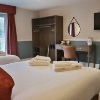 Bright, cosy hotel room with twin beds, desk, and scenic window view.