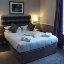 Cosy hotel room with a double bed, soft pillows, fresh towels, and warm lighting in Balmacara.