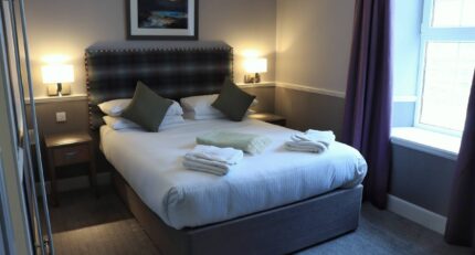 Cosy hotel room with a double bed, soft pillows, fresh towels, and warm lighting in Balmacara.