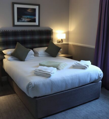 Cosy hotel room with a double bed, soft pillows, fresh towels, and warm lighting in Balmacara.
