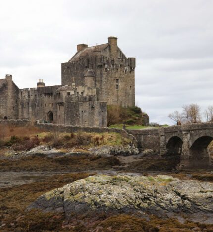 A stunning stone castle with an arched bridge set against a serene, rocky landscape near Balmacara.
