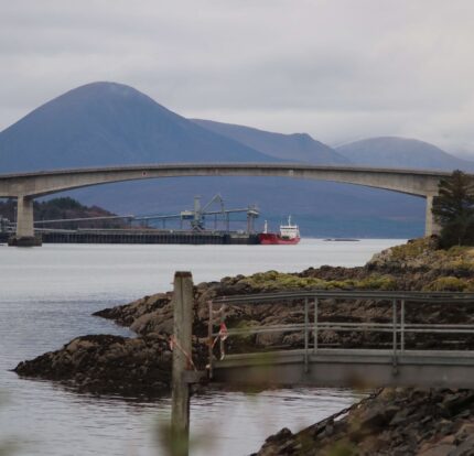 Scenic view of Skye Bridge over water, framed by rocky shores and distant mountains.