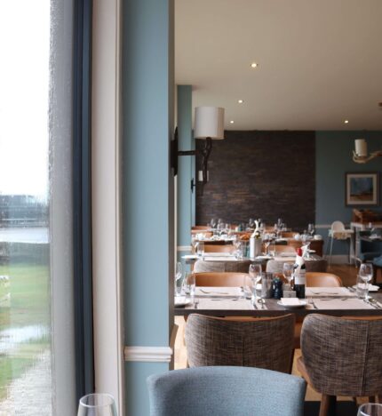 Cosy hotel dining area with elegant tables set for guests, overlooking a rainy garden view.