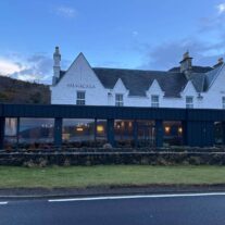 The Balmacara Hotel with warm, inviting lighting against a scenic hillside backdrop at dusk.