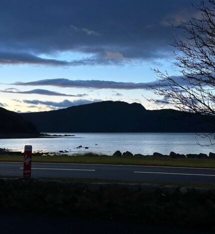 Tranquil lake view at dusk with silhouetted hills and a quiet roadside in Balmacara.