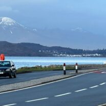 Scenic coastal view from Balmacara with mountains, sea, and parked car along a quiet road.