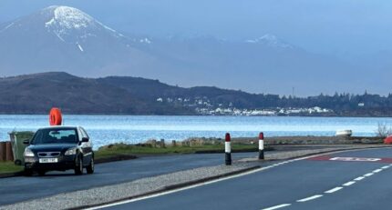 Scenic coastal view from Balmacara with mountains, sea, and parked car along a quiet road.