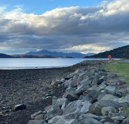 Scenic view of rocky shoreline with distant mountains under a cloudy sky near Balmacara Hotel.