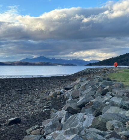 Scenic view of rocky shoreline with distant mountains under a cloudy sky near Balmacara Hotel.