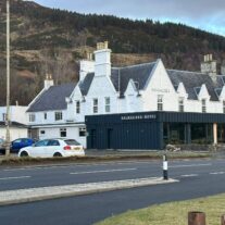 Charming Balmacara Hotel with scenic hill backdrop on a tranquil day.