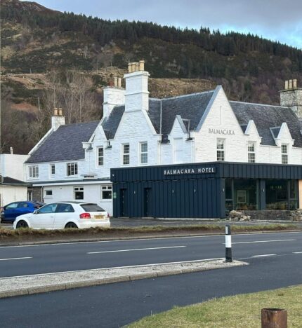 Charming Balmacara Hotel with scenic hill backdrop on a tranquil day.